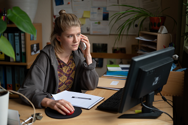 Foto einer weiblichen Person, die vor einem PC sitzt und telefoniert